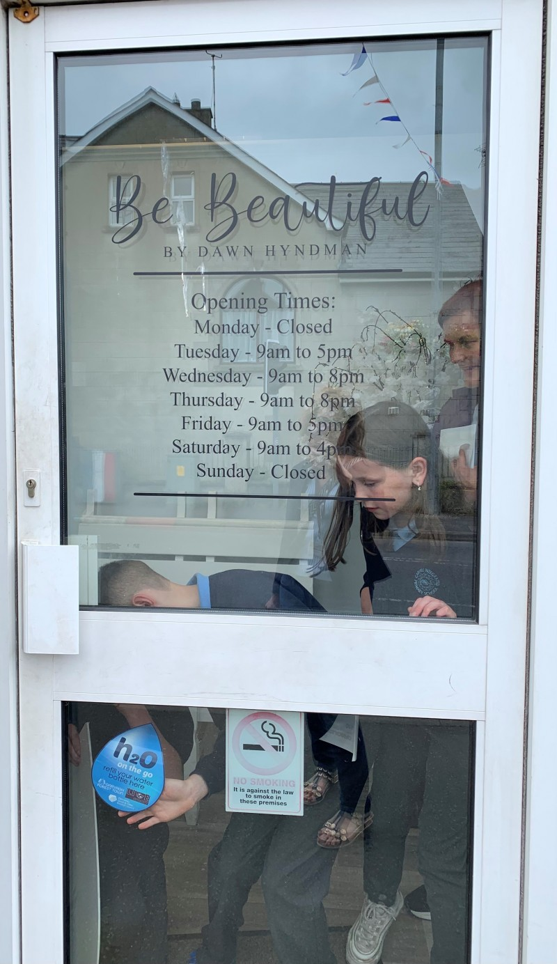 Pupils place a H20 On The Go sticker on the door of Be Beautiful beauty salon in Garvagh.