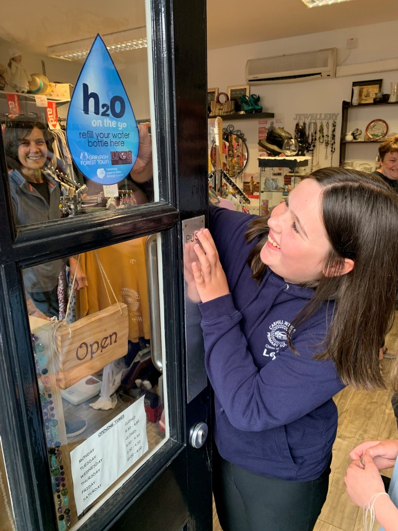 A pupil places a H20 On The Go sticker on the door of The Changing Room in Garvagh to highlight its participation in the H20 On The Go scheme.