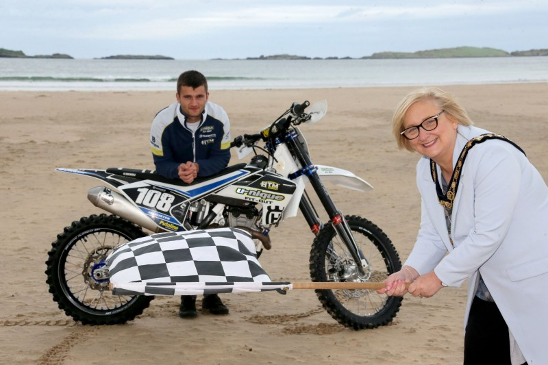 The Mayor of Causeway Coast and Glens Borough Council Councillor Brenda Chivers waves the chequered flag as she joins Ballymoney racer Michael McAlister at East Strand ahead of Portrush Beach Races which return to the resort on October 27th and 28th.