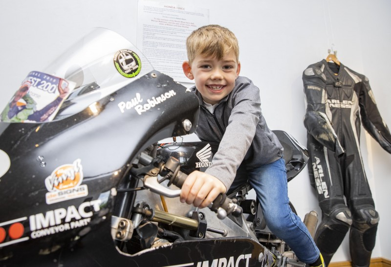Young Bobby Acheson enjoys his time on the bike that helped Paul Robinson win the NW200. The bike was brought along to launch the new NW200 photographic exhibition at Roe Valley Arts and Cultural Centre. Available until 20th August 2022, it features historic racing photos from the book ‘NW200 90th Road & Race’.