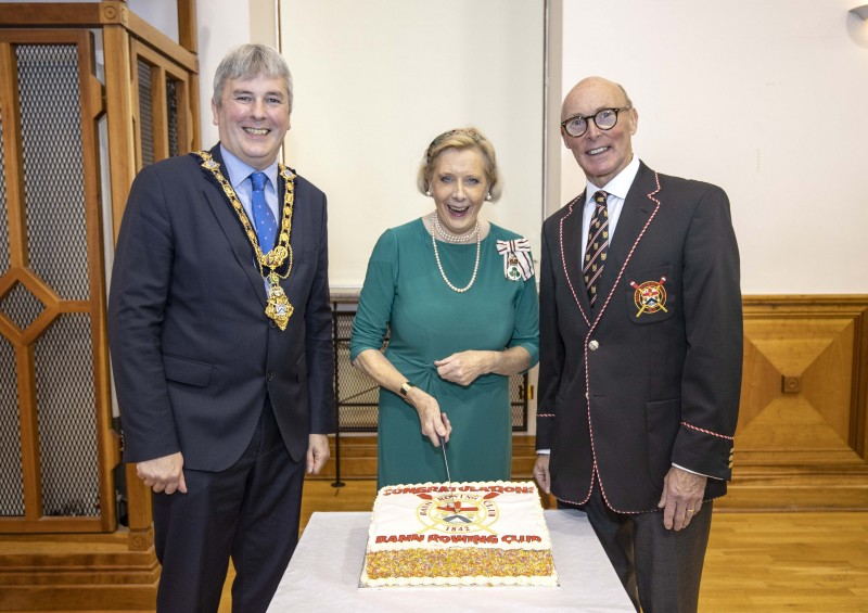 Lord-Lieutenant for County Londonderry Alison Millar cuts a special cake to mark the presentation of the Queen’s Award for Voluntary Service to Bann Rowing Club alongside the Mayor of Causeway Coast and Glens Borough Council Councillor Richard Holmes and Bann Rowing Club Captain Keith Leighton.
