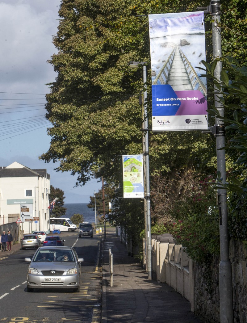 Street banners on Quay Road in Ballycastle showcasing Bonamargy Friary and Knocklayde mountain by Bena Breslin and the Pans Rocks by Raeanne Lowry.