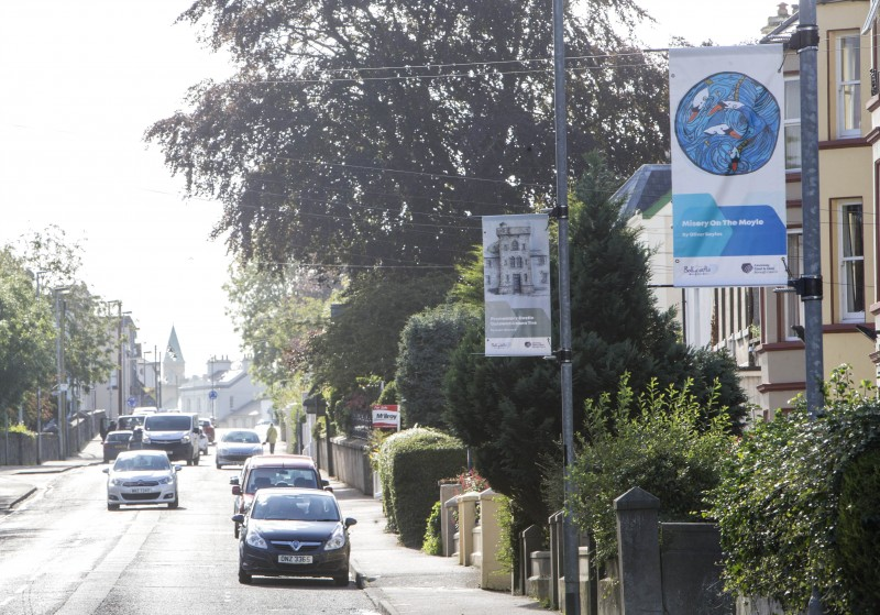 Street banners on Quay Road in Ballycastle showcasing ‘Misery on the Moyle by Oliver Bayles and Promontory Castle by Louie Winward.