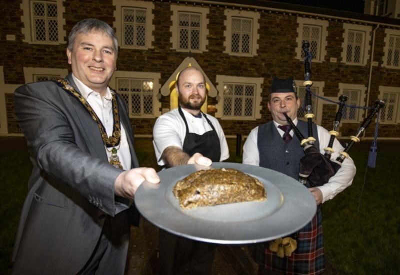 The Mayor of Causeway Coast and Glens Borough Council Councillor Richard Holmes presents the haggis at the Burns Night event held in Limavady with chef Curtis McDaid and piper Darren Milligan.