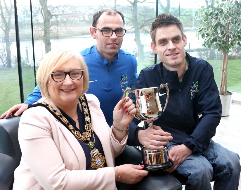 Paul McLister, the first person from Northern Ireland to win the Irish National BC4 Boccia Championship, shows his winning trophy to the Mayor of Causeway Coast and Glens Borough Council Councillor Brenda Chivers alongside Odhran Doherty, Boccia Performance Pathway Officer & Lead Coach from Disability Sport NI.