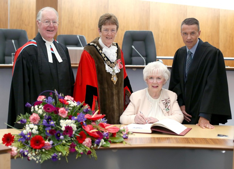 Mrs Joan Christie CVO OBE signs the Freedom register at her Freedom of the Borough ceremony alongside the Mayor of Causeway Coast and Glens Borough Council Councillor Joan Baird OBE, Council Chief Executive David Jackson and the Mayor's Chaplain the very Reverend Godfrey Brown.
