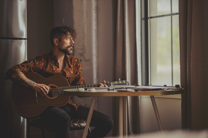 Singer-songwriter Niall McCabe will wow audiences at Roe Valley Arts Centre on Saturday 11 May. Niall pictured here sitting looking out a window as he plays his guitar.