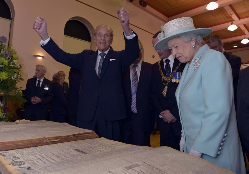 2014, The Queen and Prince Philip look at articles from archive newspaper editions of the Chronicle/Constitution in Coleraine Town Hall.